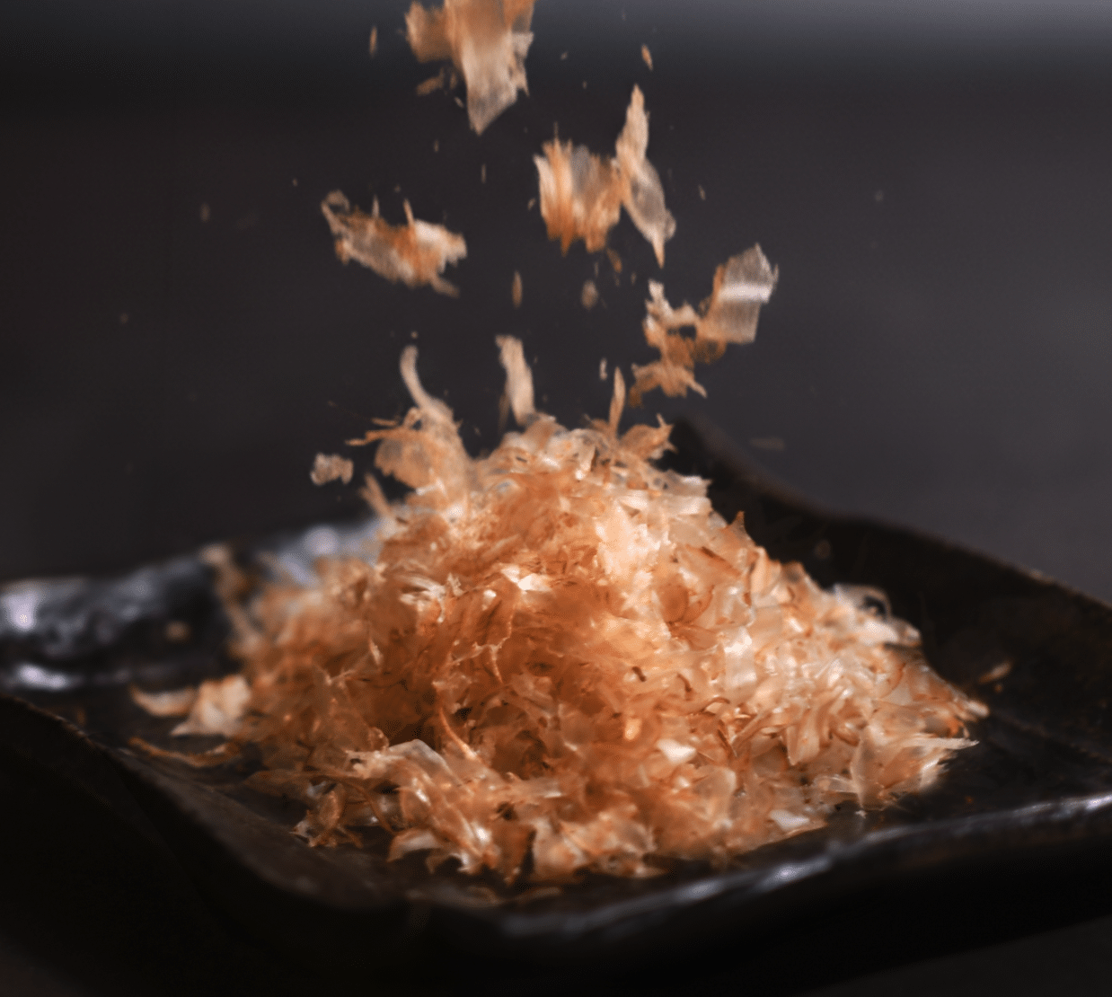 オーク材の薪炭火で燻し、薄く削り出したベーコン節®が黒い皿に舞い落ちる様子
